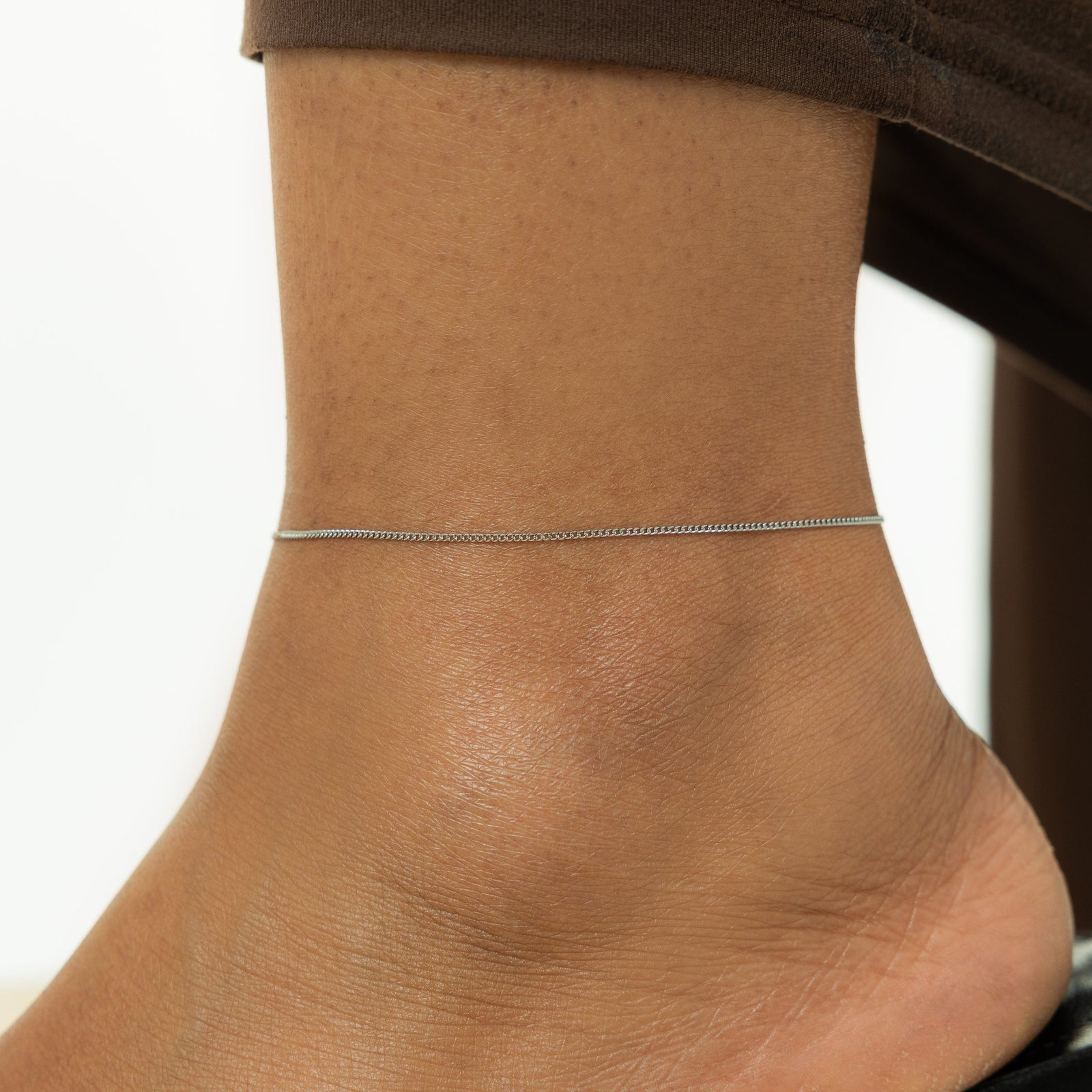 Close up of the silver Micro Curb Anklet as worn by the model.