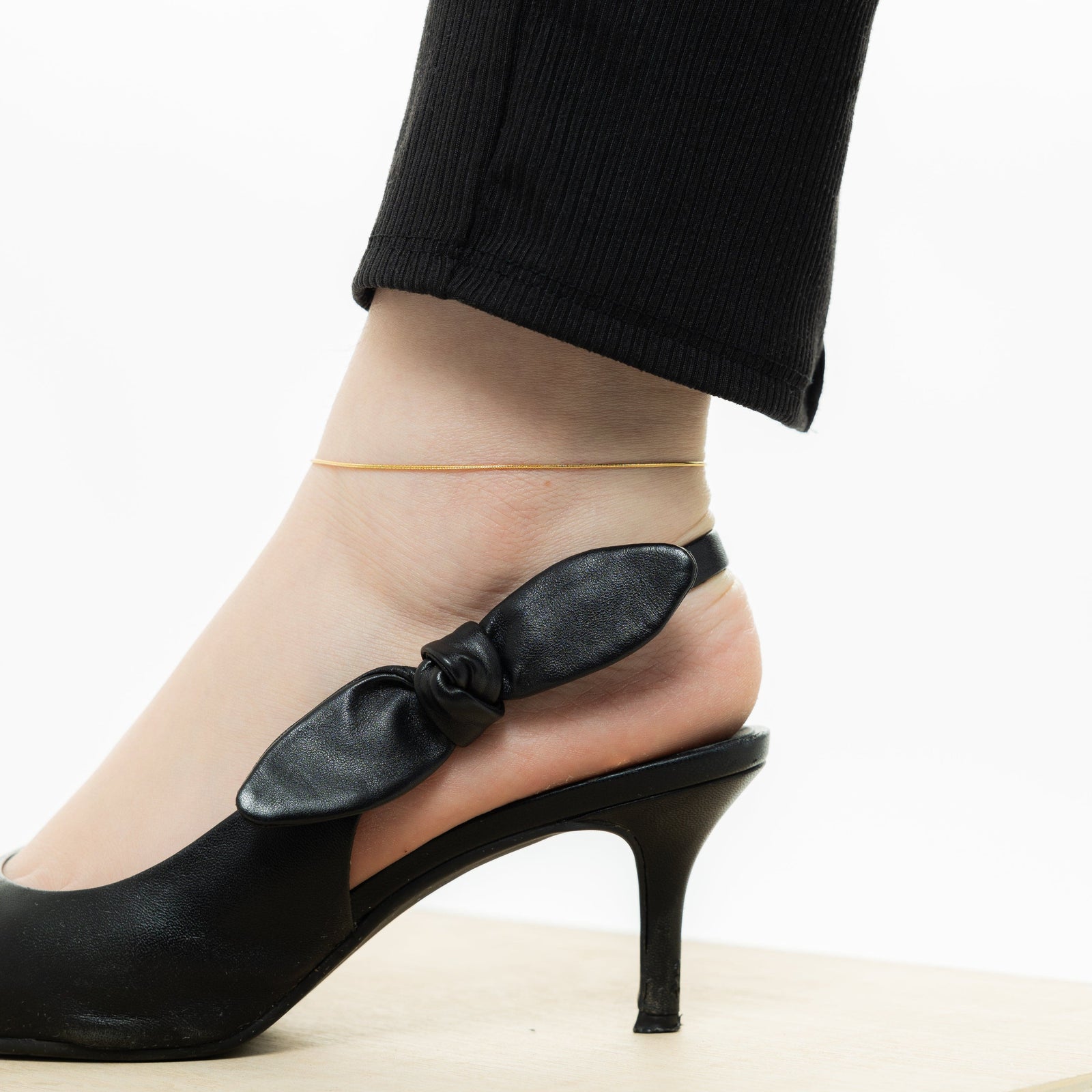 Photo of the model's left foot wearing the gold Micro Harmony Anklet and slip on sandals.