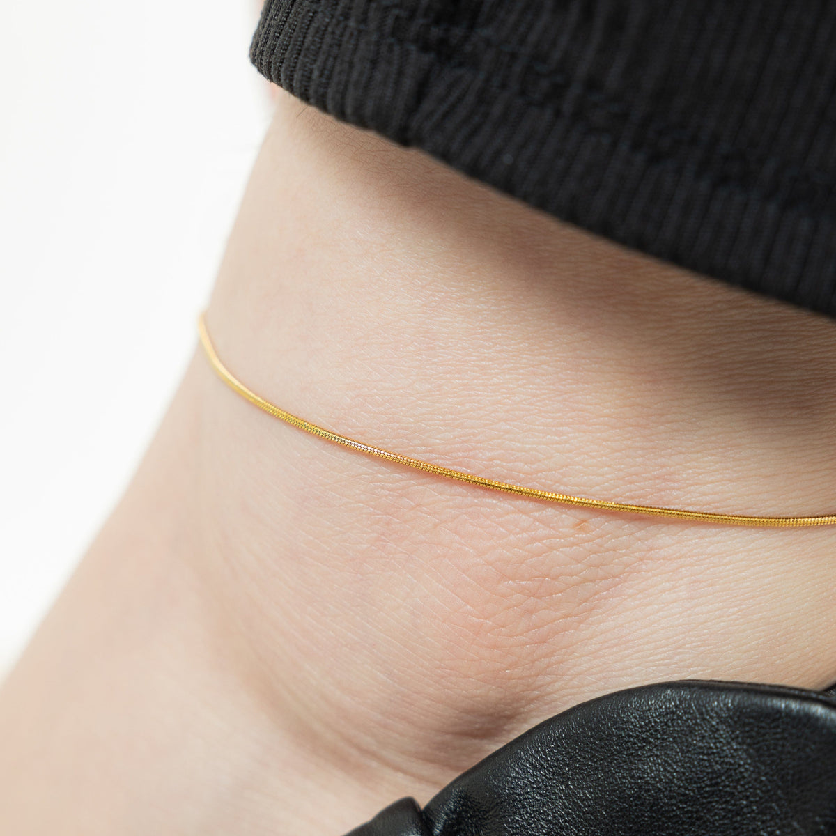 Close up of the gold Micro Harmony Anklet as worn by the model.