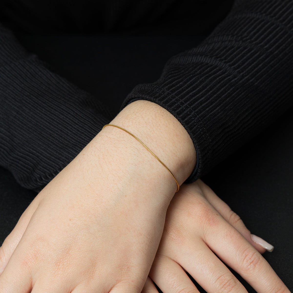 Close up of the model's hands. The model is wearing the gold Micro Harmony Bracelet on their left wrist.