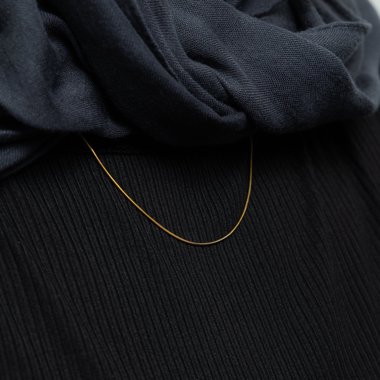 The gold Micro Harmony Chain against the black fabric of the model's clothing.