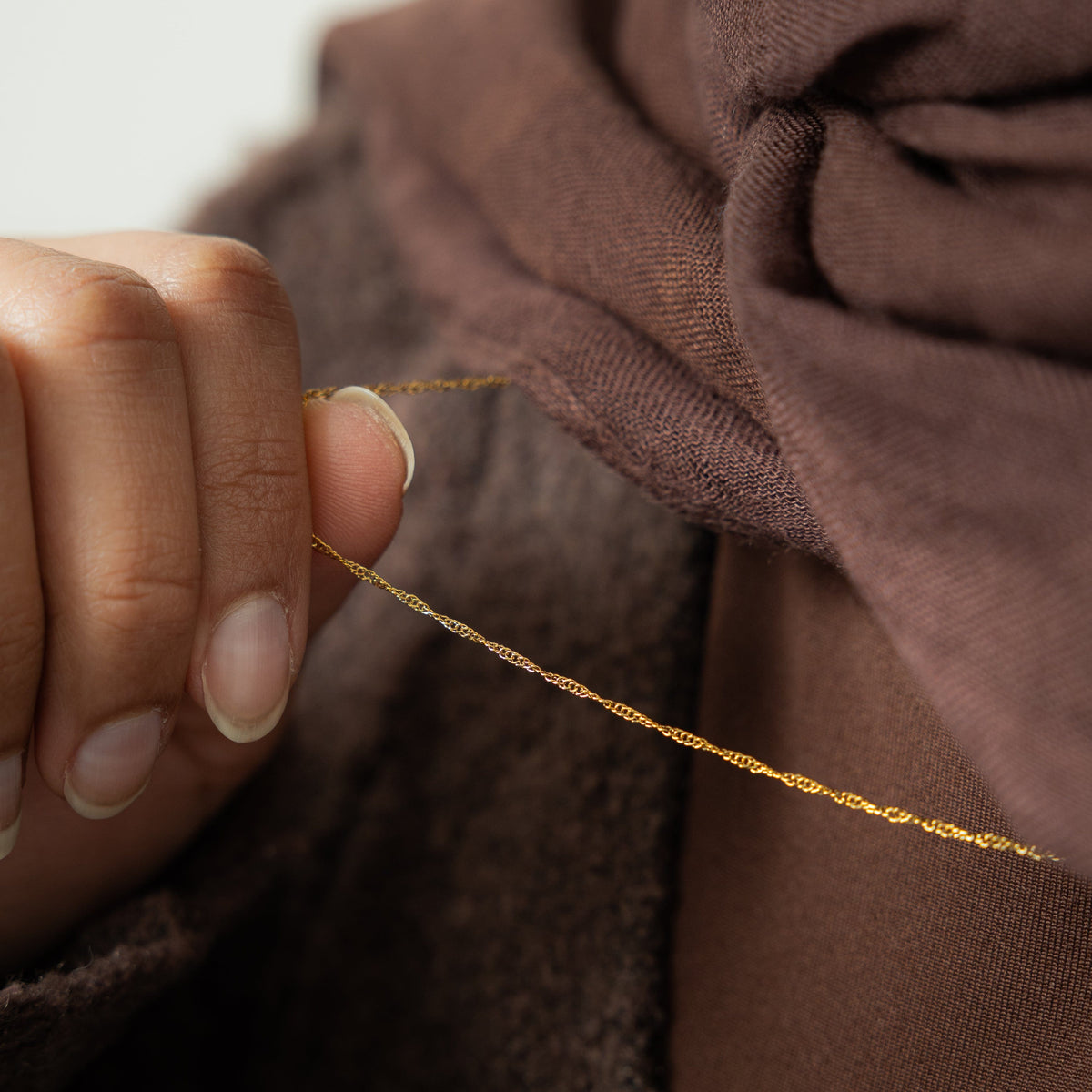 Close up of the gold Micro Twisted Chain as the model holds the chain between their fingers.