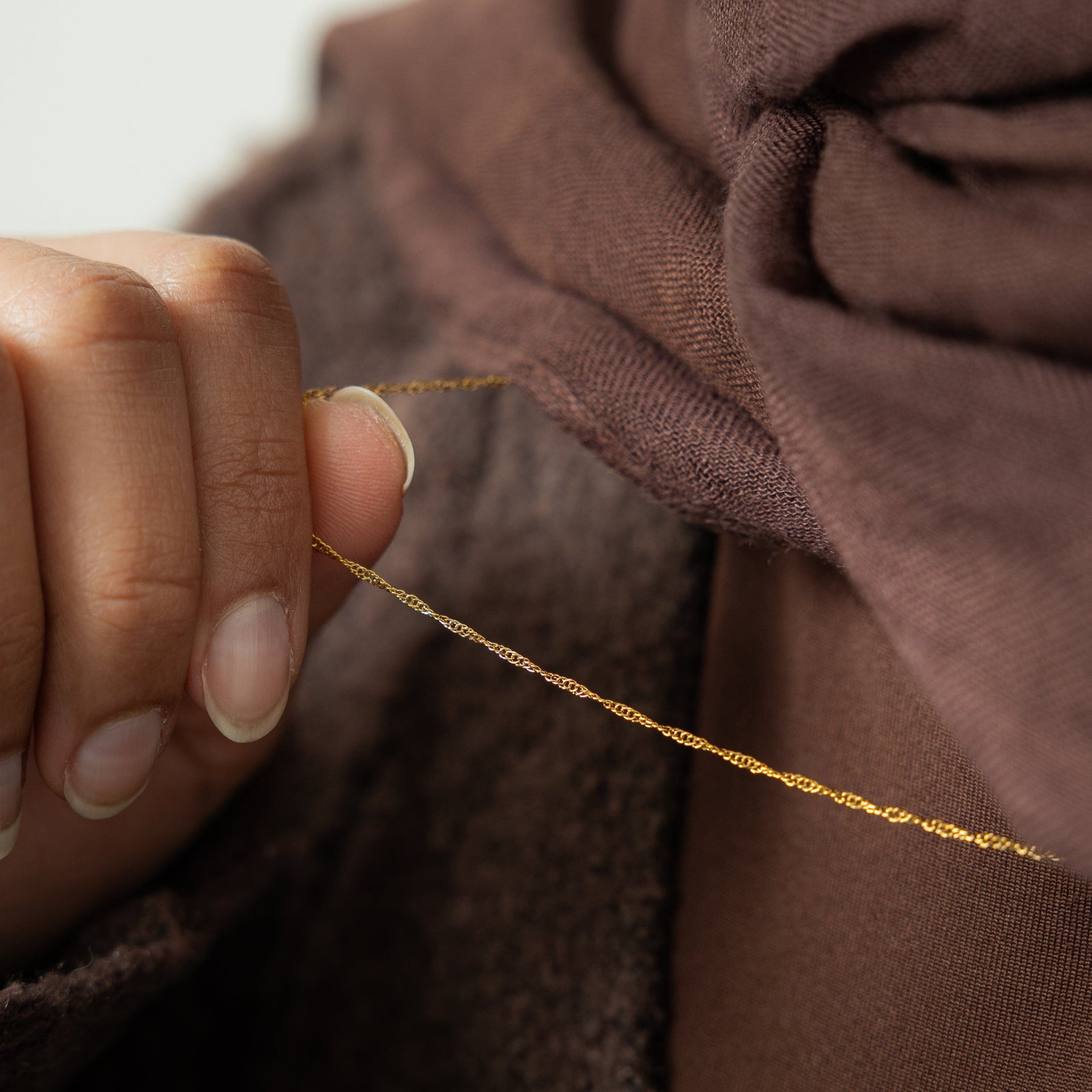Close up of the gold Micro Twisted Chain as the model holds the chain between their fingers.