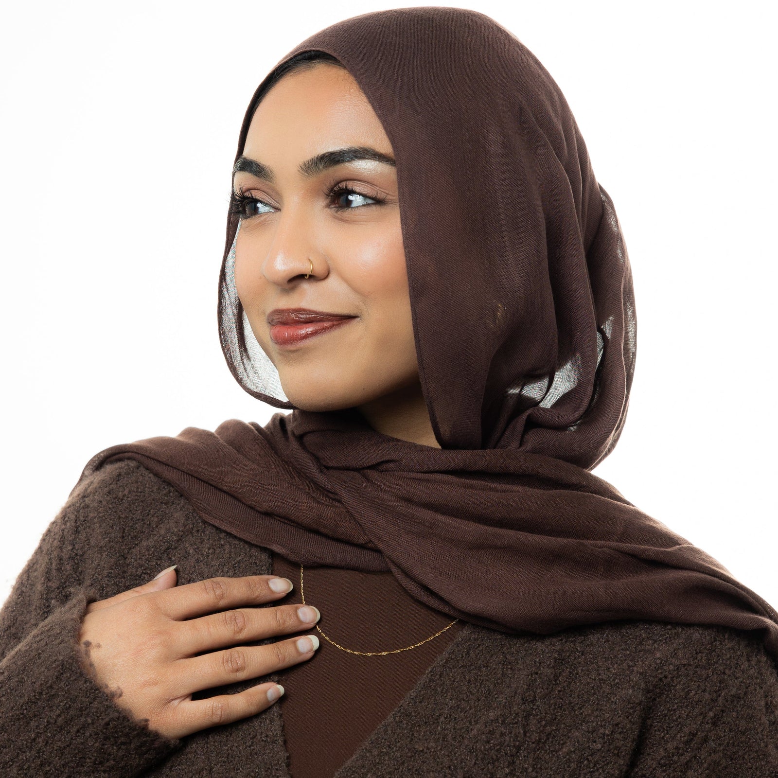 Photo of the model looking away from the camera and smiling, the model is also touching the gold Micro Twisted Chain they are wearing.