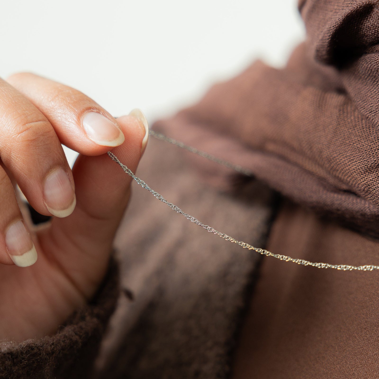 Close up of the silver Micro Twisted Chain as the model holds it between their fingers.