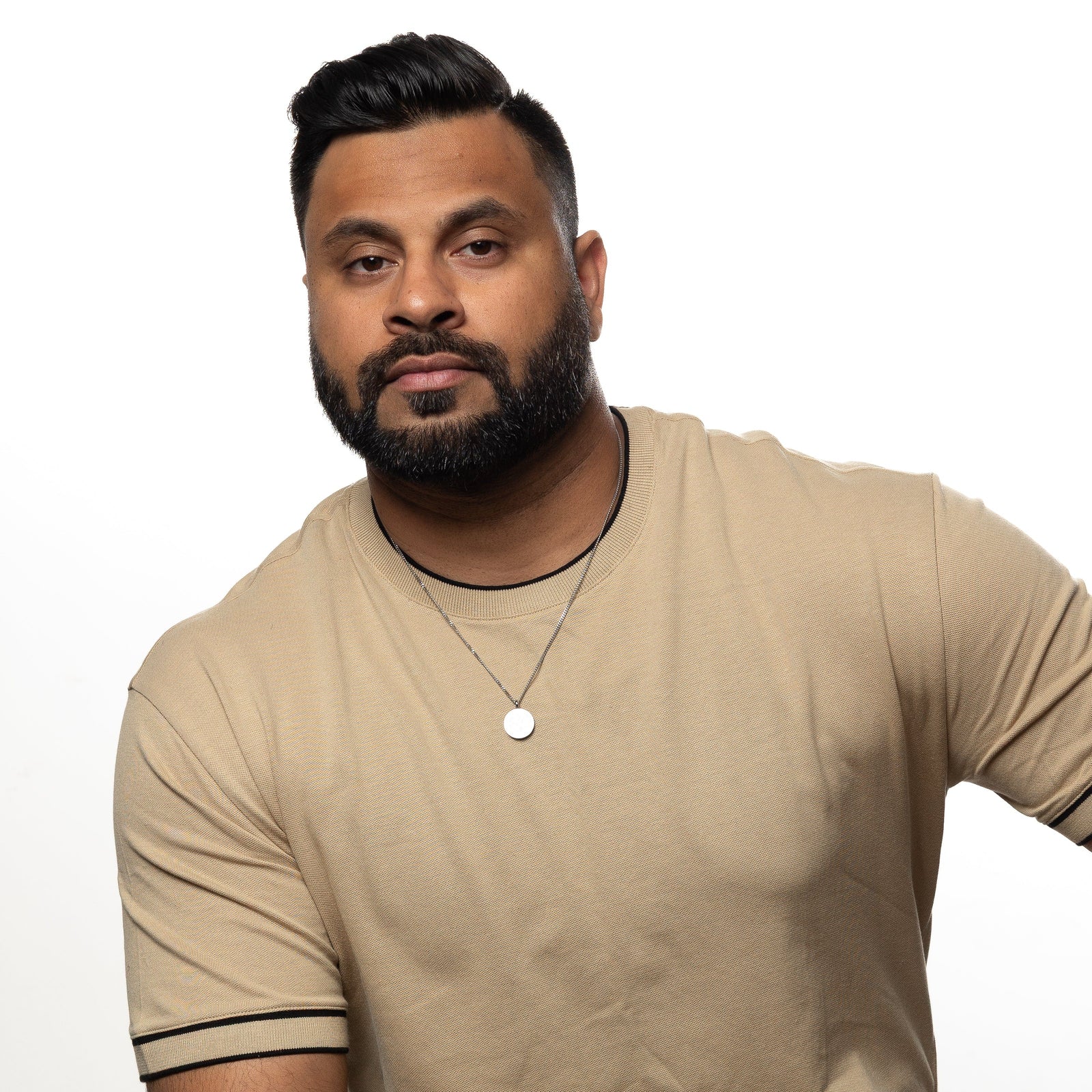 Man wearing a silver 'Maktub' token necklace over a beige shirt.