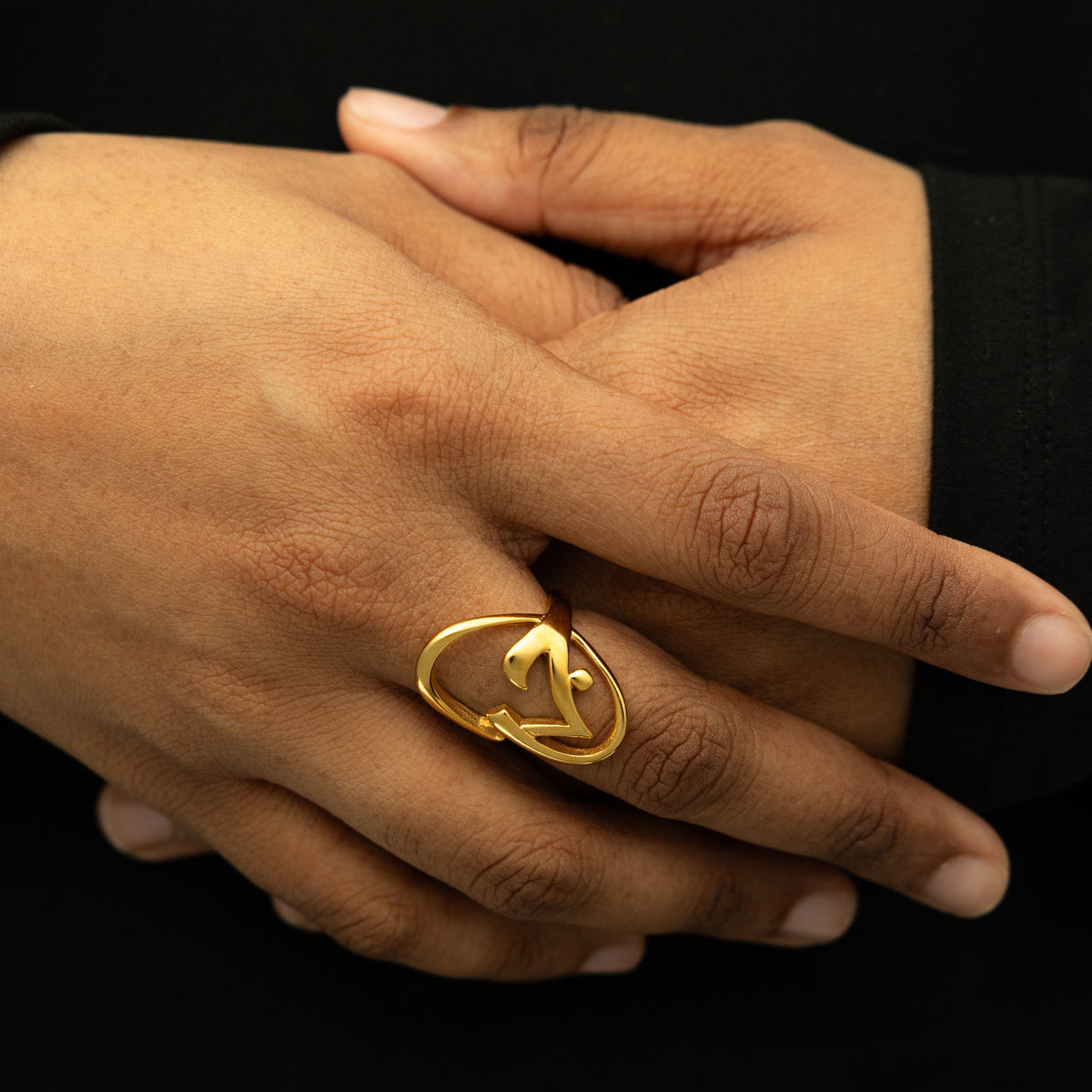 Close-up of the gold Jaan Ring worn on hand, showing the open oval shape with curved calligraphy detailing.