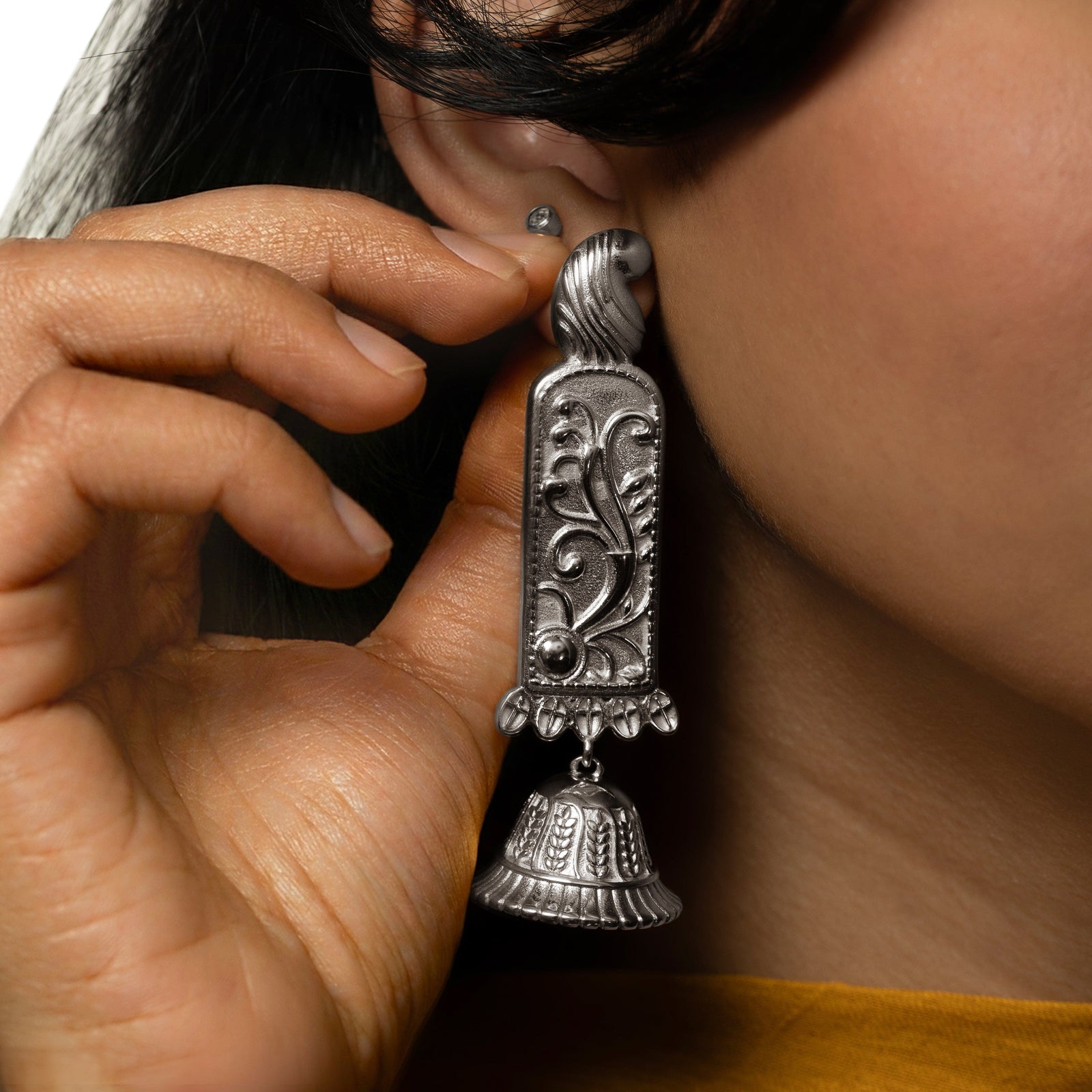 Model touching the gold Jhumka Paisley Earrings worn on their right ear.