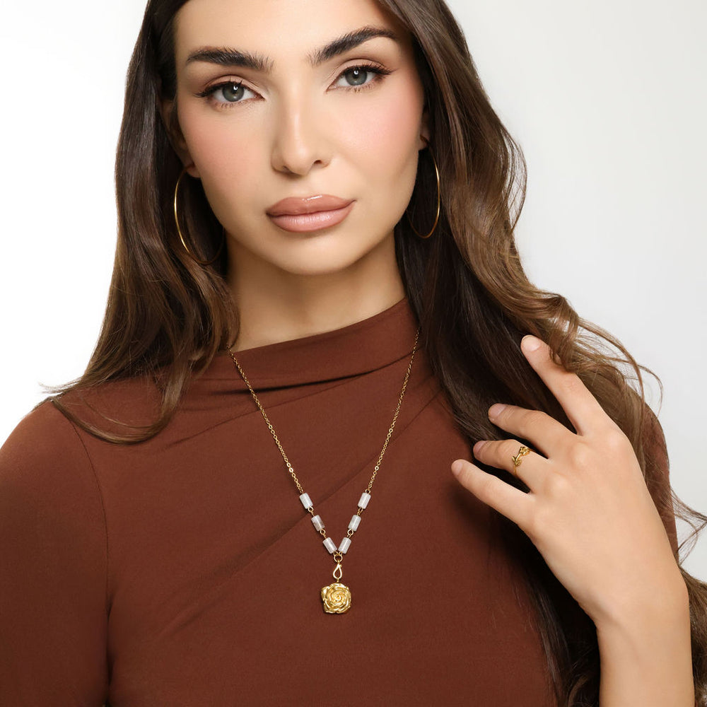 Woman wearing an 18k gold plated necklace with a detailed rose flower pendant and milky white tube beads, paired with gold hoop earrings and a ring.