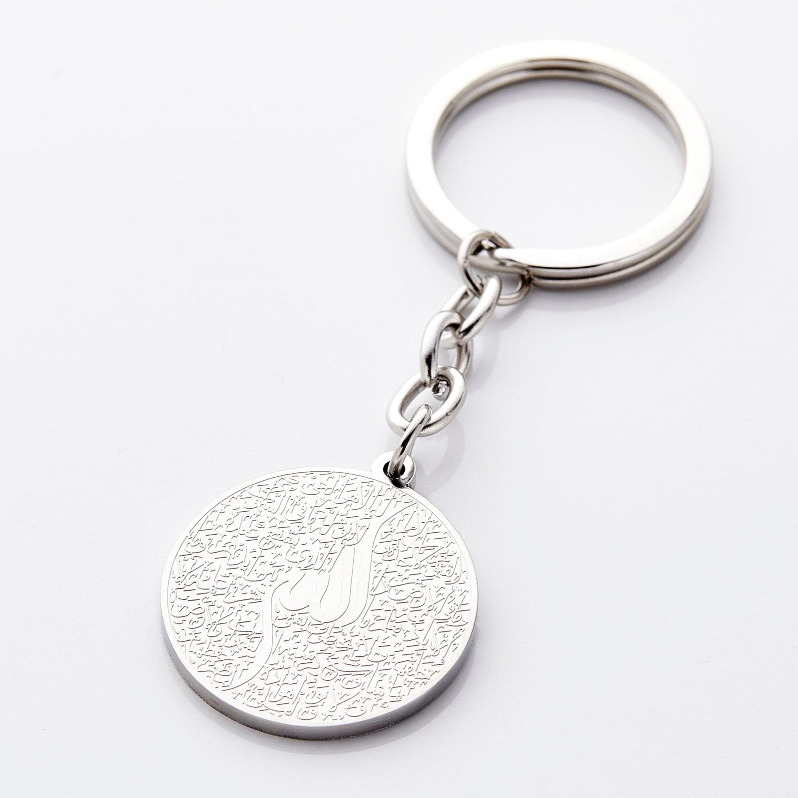 Photo of a silver keychain with a round pendant that contains a see-it-to-believe it intricate engraving of the entire verse of Ayatul Kursi