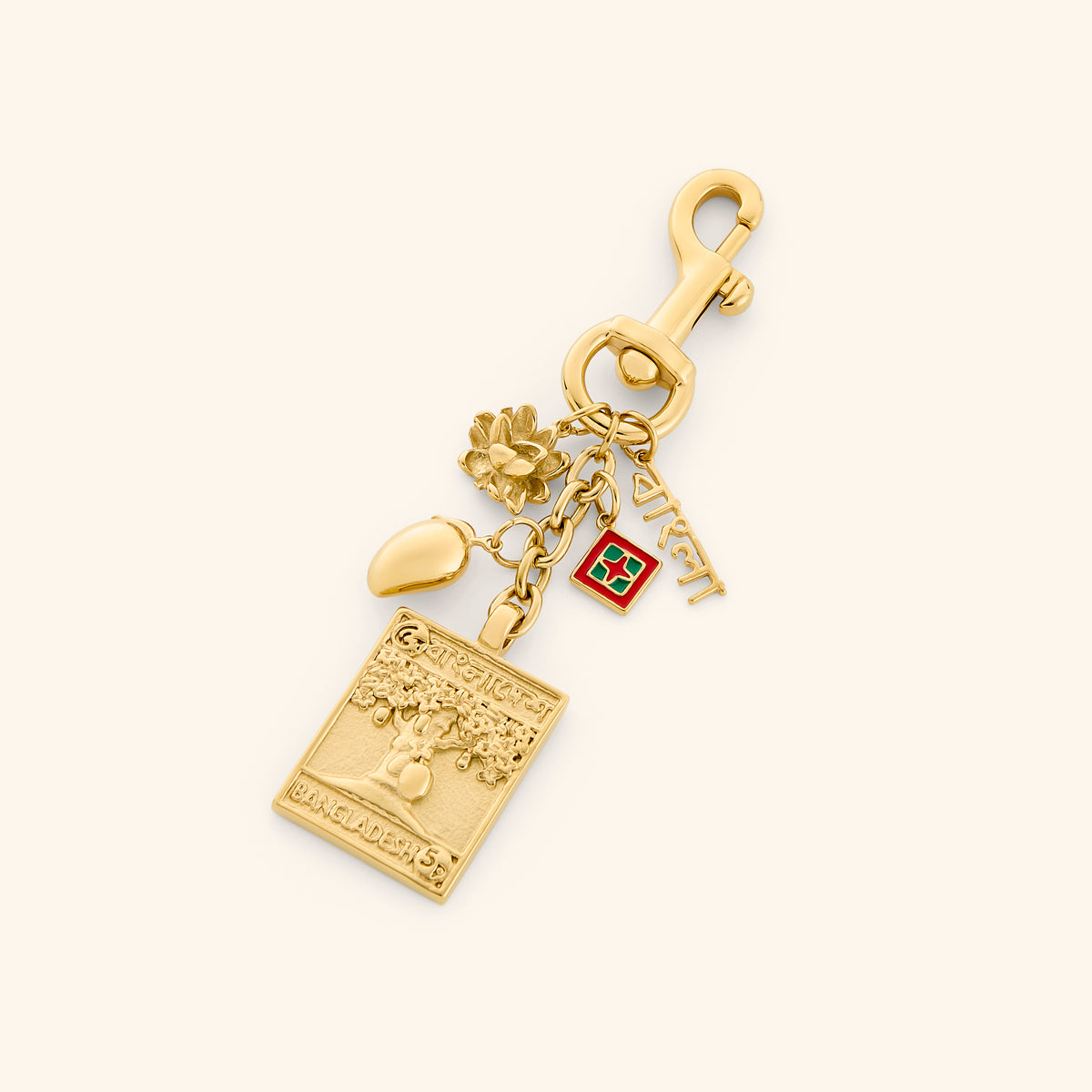 The Bangladesh Stories Bag Charm by Nominal, crafted with an 18k gold-plated finish featuring cultural charms including an embossed Bengal tiger postage stamp, water lily, and Bengali script, displayed on an off-white background.