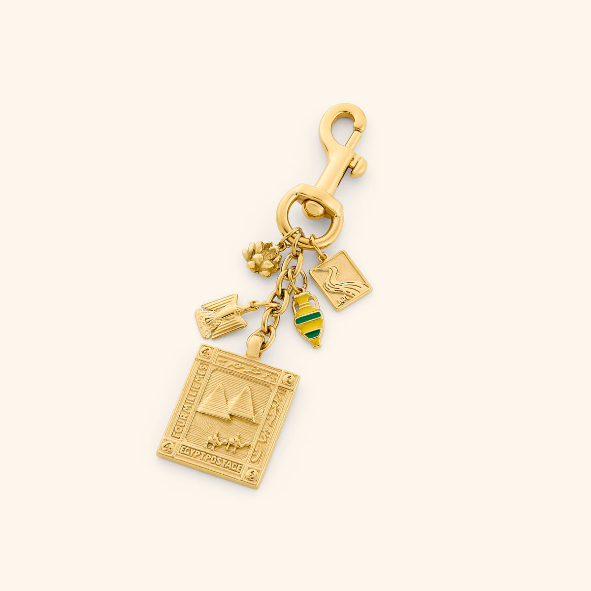 The Egyptian Stories Bag Charm by Nominal, crafted with an 18k gold-plated finish featuring cultural charms including an embossed Pyramids of Giza postage stamp, lotus flower, and iconic heritage pendants, displayed on an off-white background.