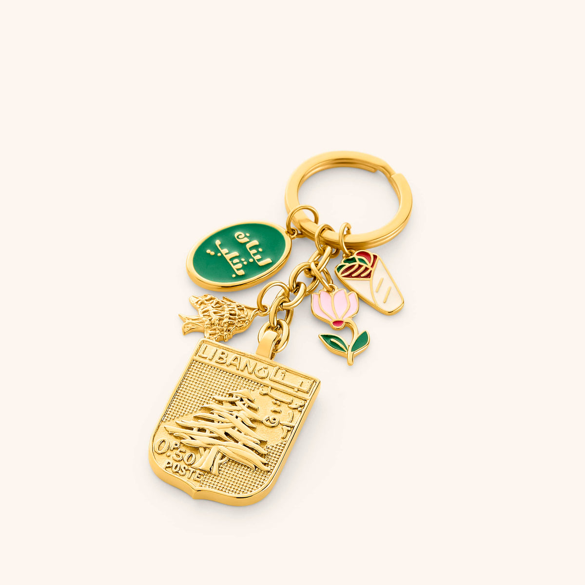The Lebanon Stories Bag Charm by Nominal, crafted with an 18k gold-plated finish featuring cultural charms including an embossed cedar tree postage stamp, green Arabic calligraphy medallion, and traditional heritage pendants, displayed on an off-white background.