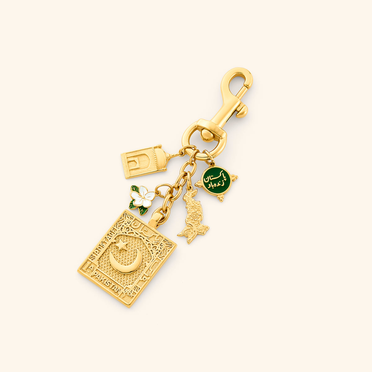 he Pakistan Stories Bag Charm by Nominal, crafted with an 18k gold-plated finish featuring heritage charms including an embossed postage stamp, green Urdu medallion, white jasmine flower, and map outline, displayed on an off-white background.