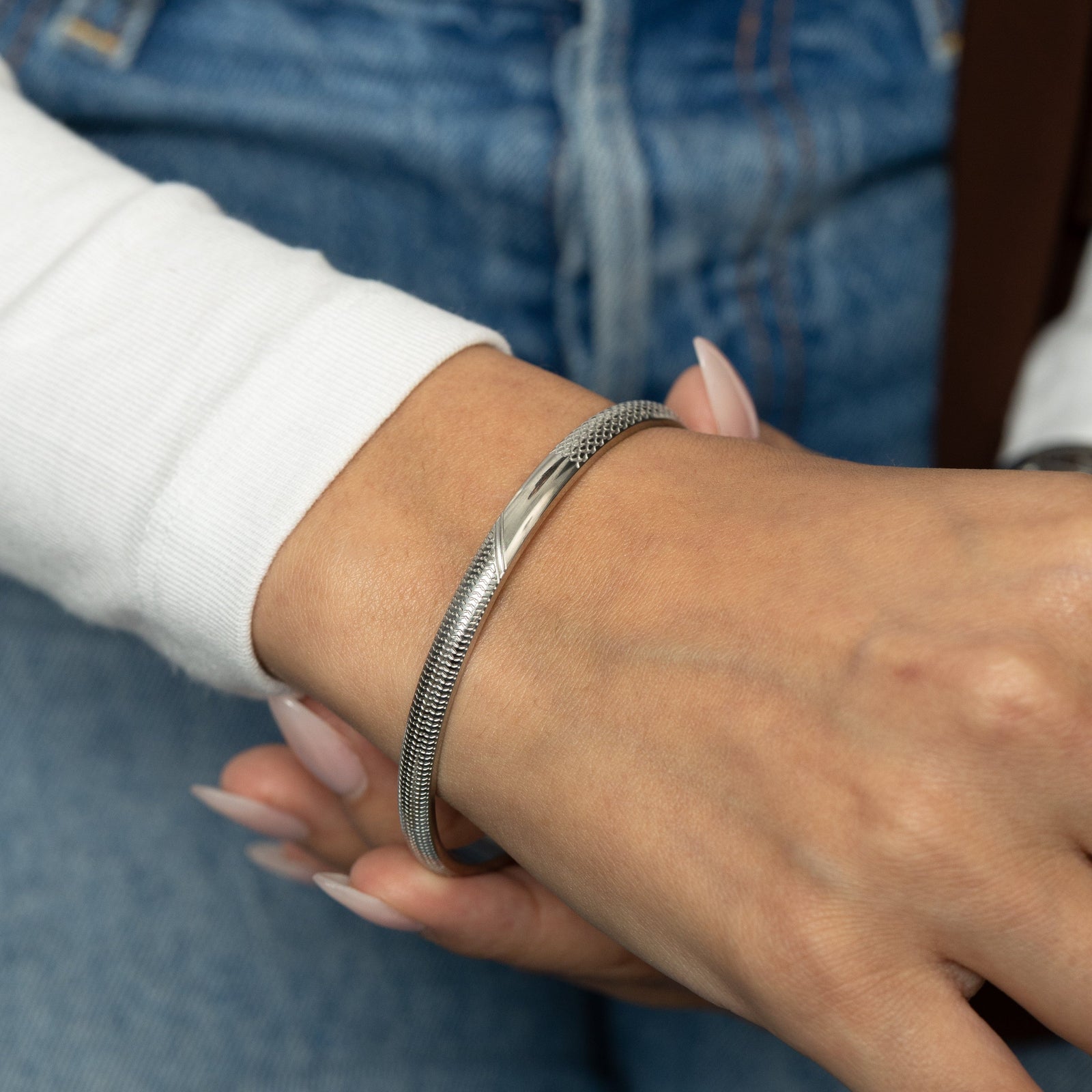 Silver keffiyeh pattern engraved bangle on a wrist.