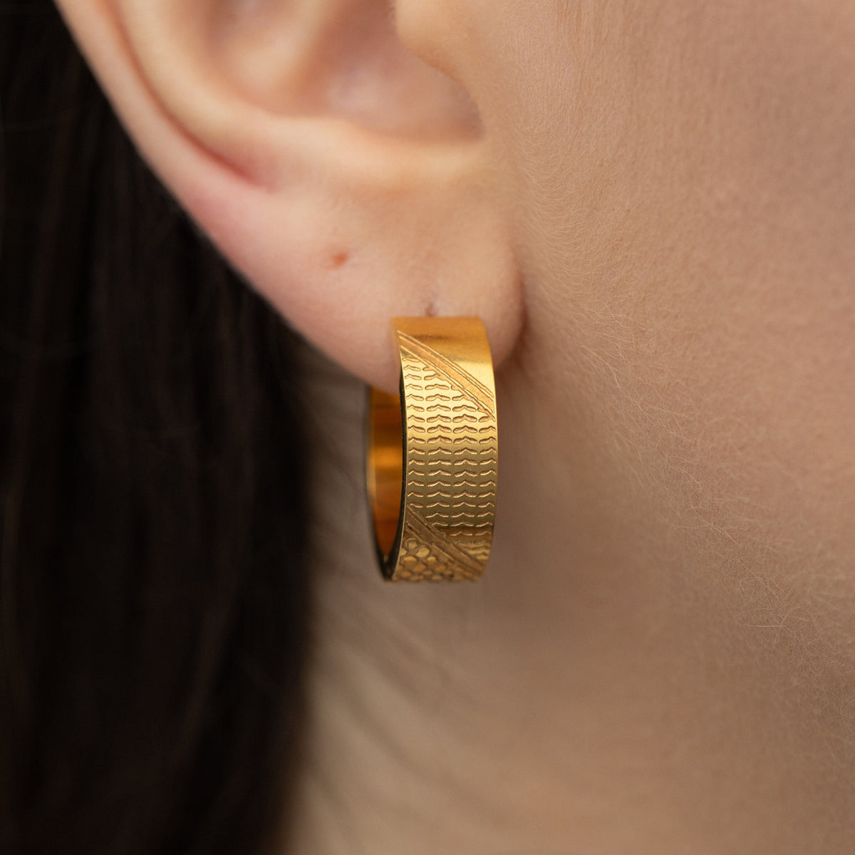 Gold keffiyeh chunky hoop worn on an ear.