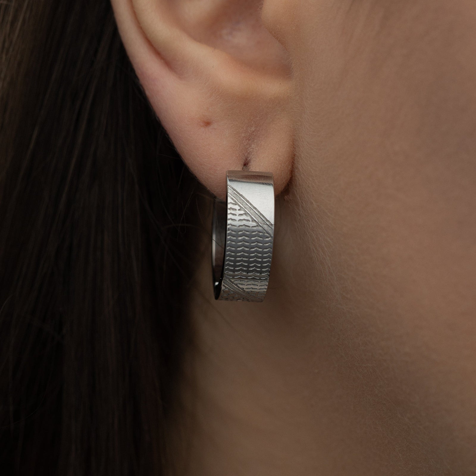Silver keffiyeh chunky hoop worn on an ear.