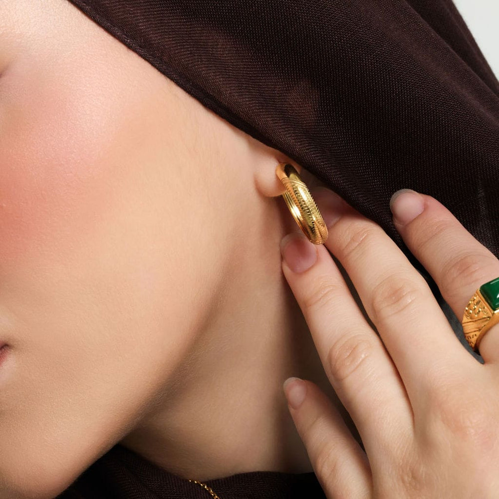 Close up of the gold Keffiyeh Mini Hoops as worn by the model on their left ear.
