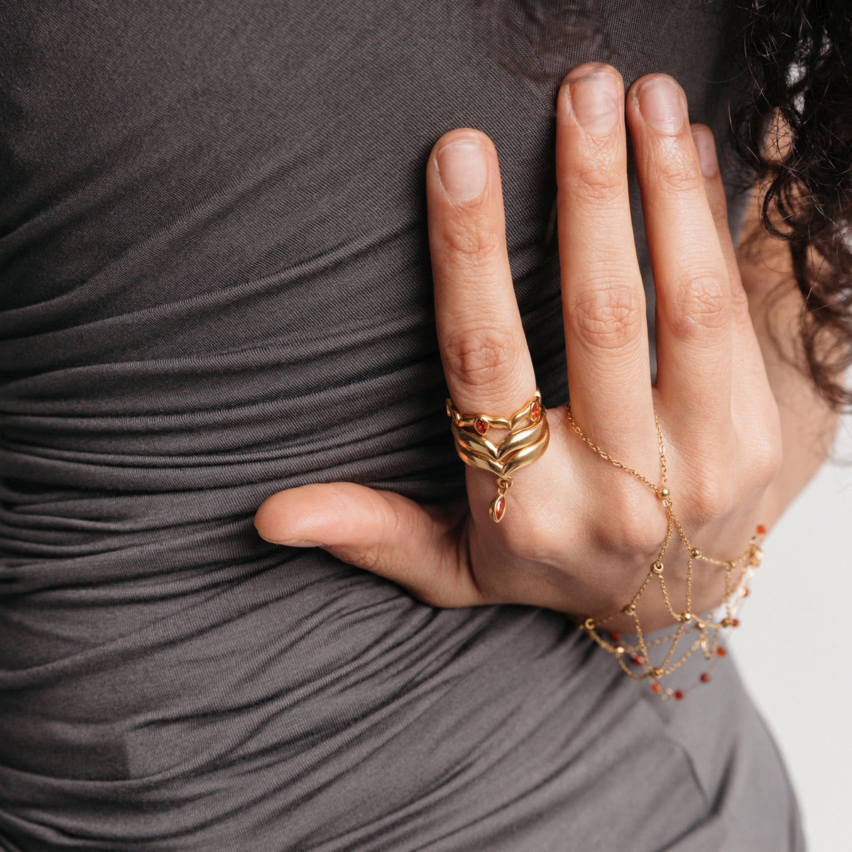 Model styled in 18k gold-plated Nominal jewelry featuring the Keffiyeh Droplet Ring Stack with garnet accents paired with the Red Bead Fishnet Hand Chain.