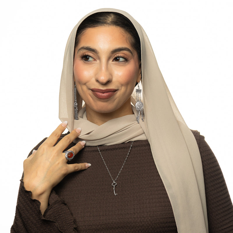 Woman wearing the silver Palestine Key of Return Necklace with a textured key pendant pimage_ styled with a beige scarf and brown top.