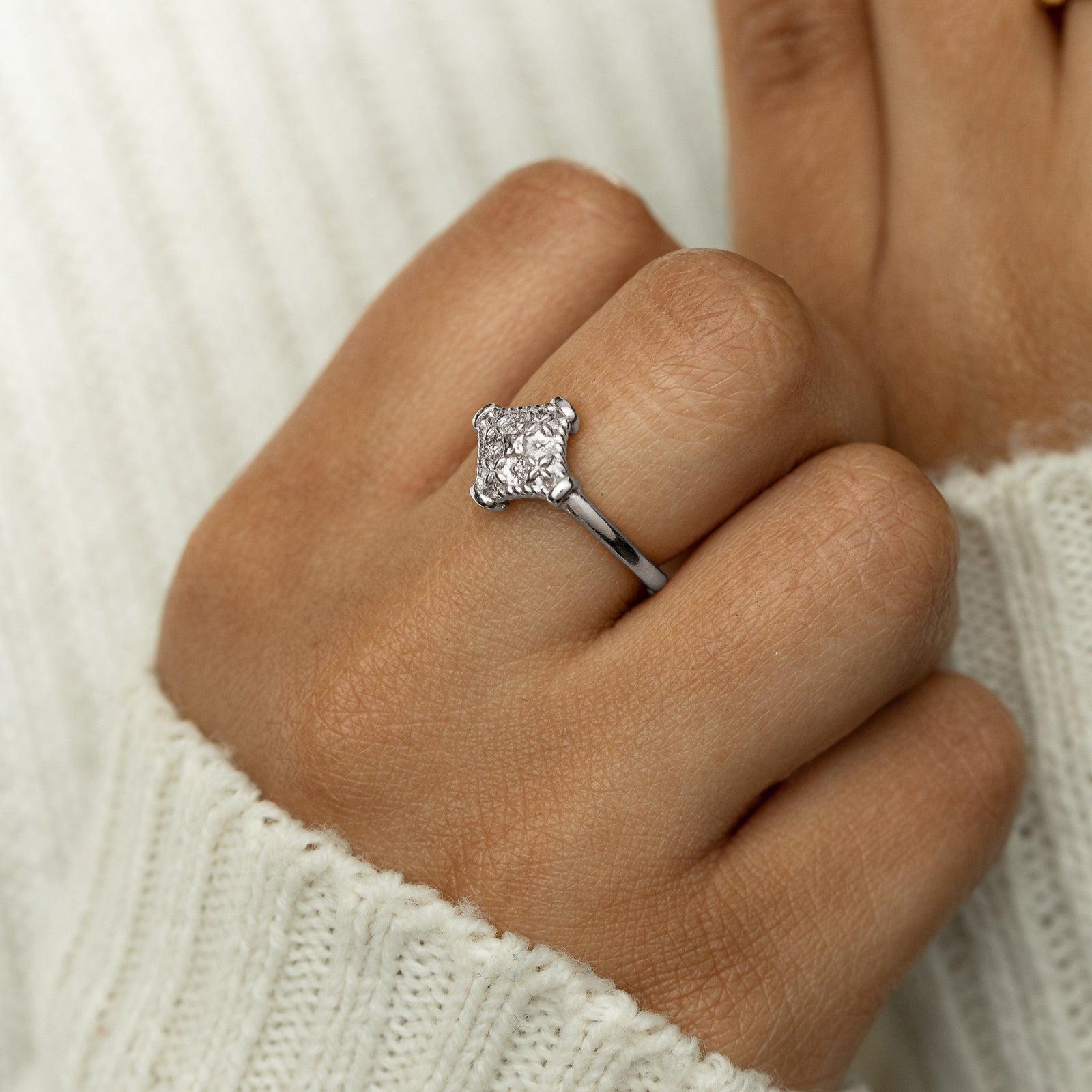 Woman wearing a silver kitework ring with a raised, textured centerpiece, styled with a cream sweater.