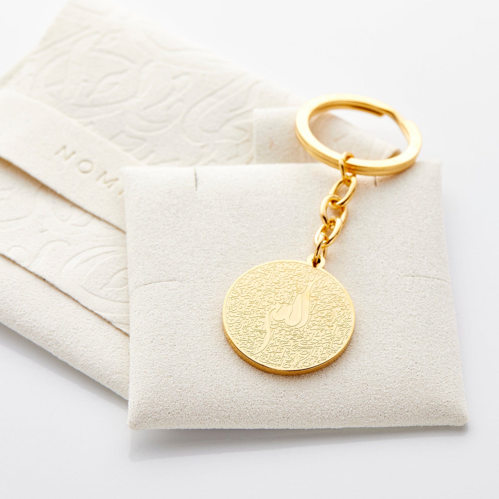 Close up of the gold Ayatul Kursi Keychain V2 resting against its velvet packaging.