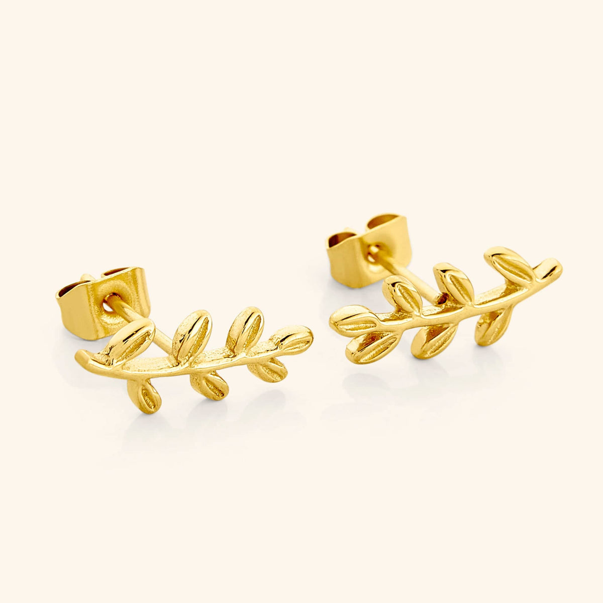 A close-up of the Olive Leaf Earrings in 18K gold plating. The earrings feature delicate olive leaf designs, symbolizing resilience and connection, suspended from hypoallergenic stainless steel posts.