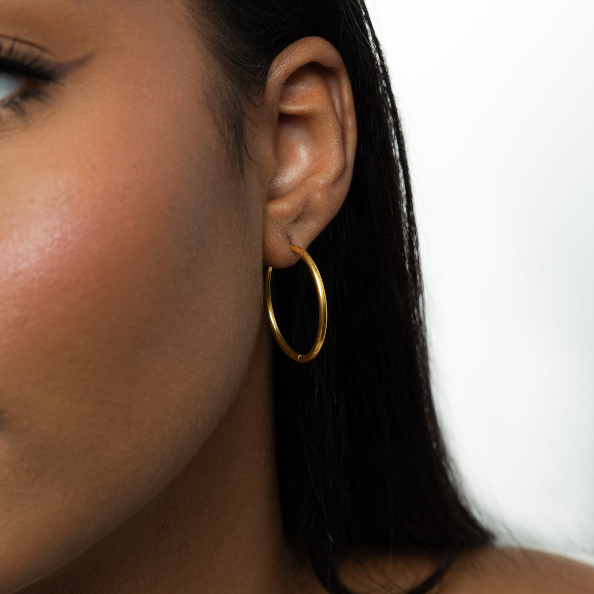 Close up of the gold Large Essential Hoops | 25mm as worn by the model on their left ear.