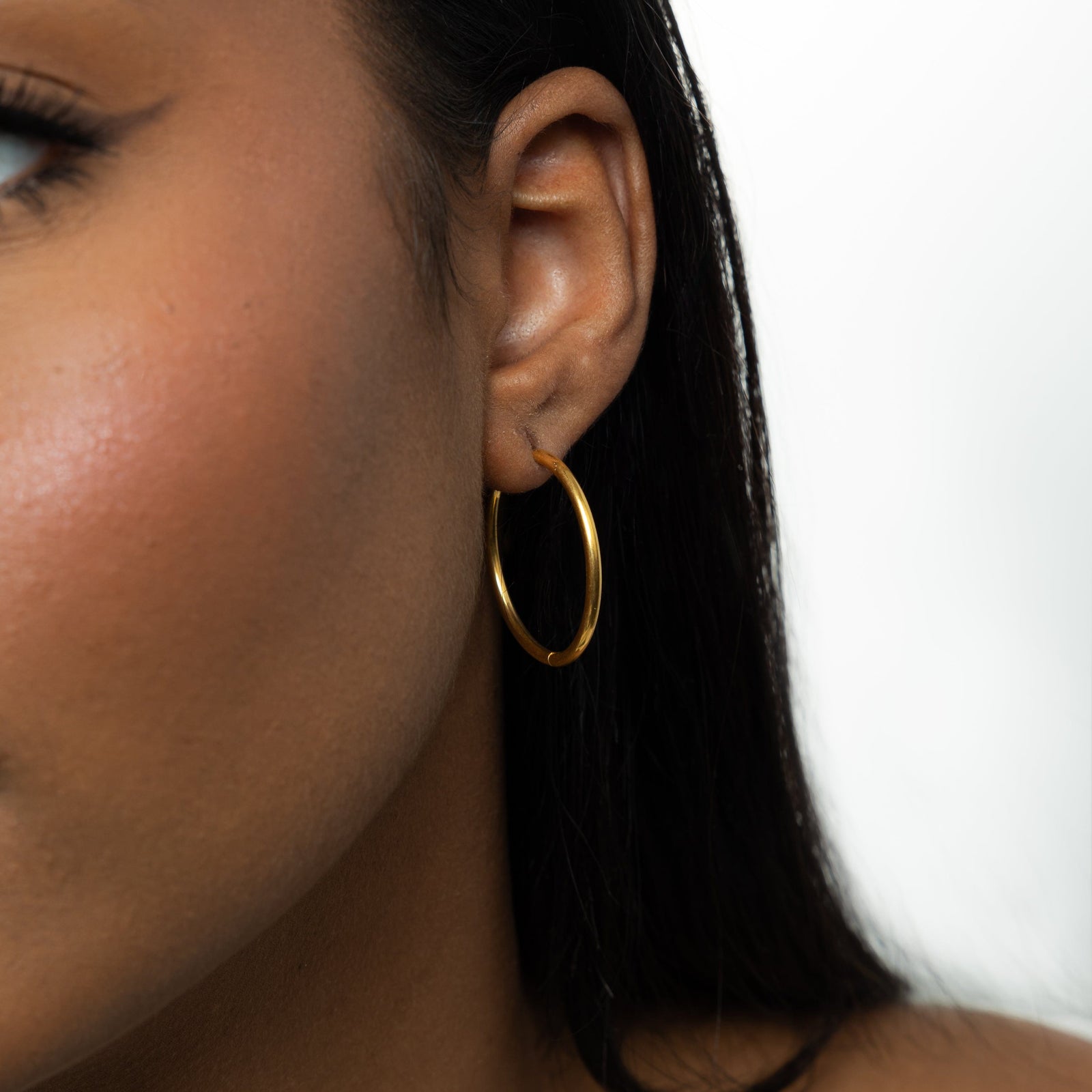 Close up of the gold Large Essential Hoops | 25mm as worn by the model on their left ear.