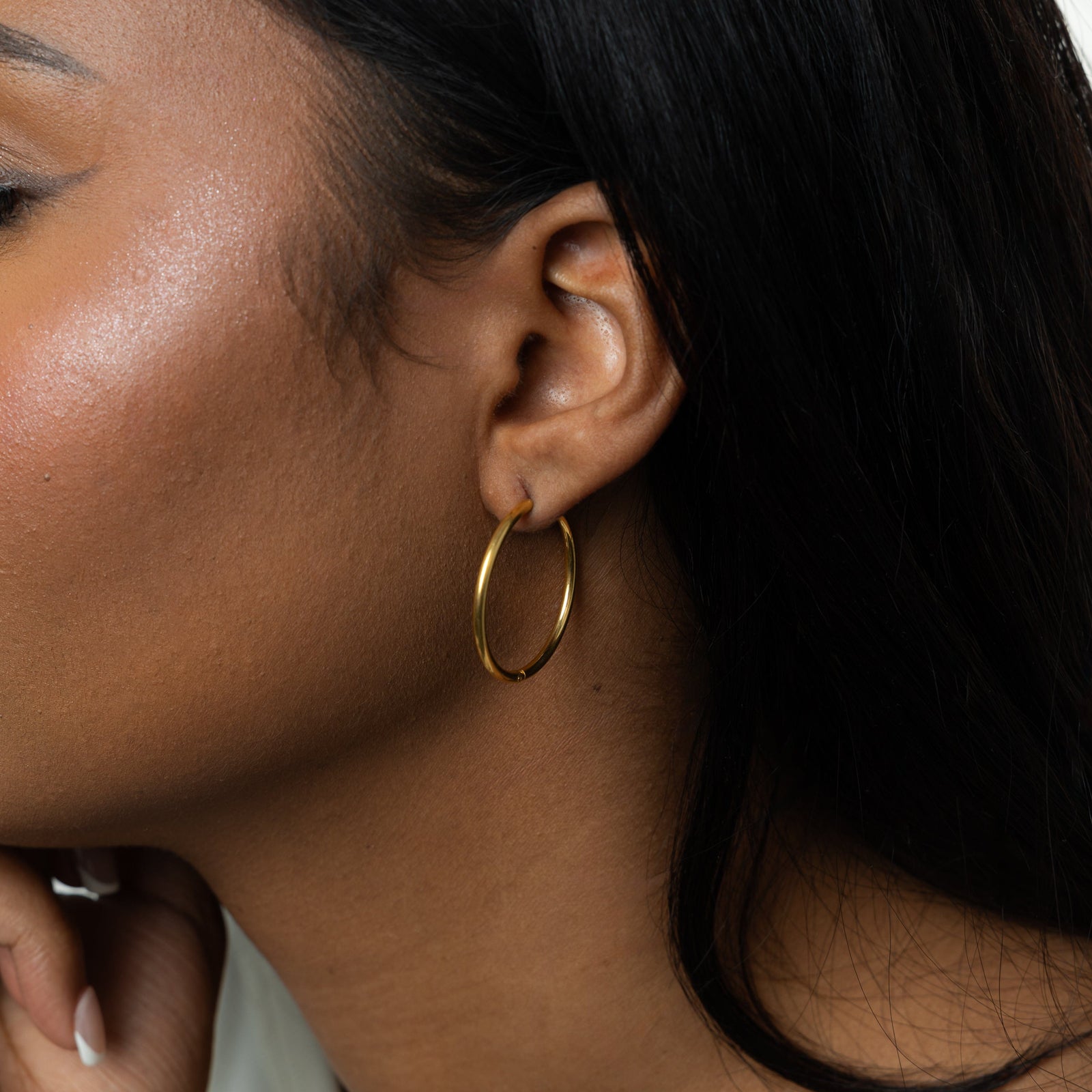 Close up of the gold Large Essential Hoops | 25mm as worn by the model on their left ear.