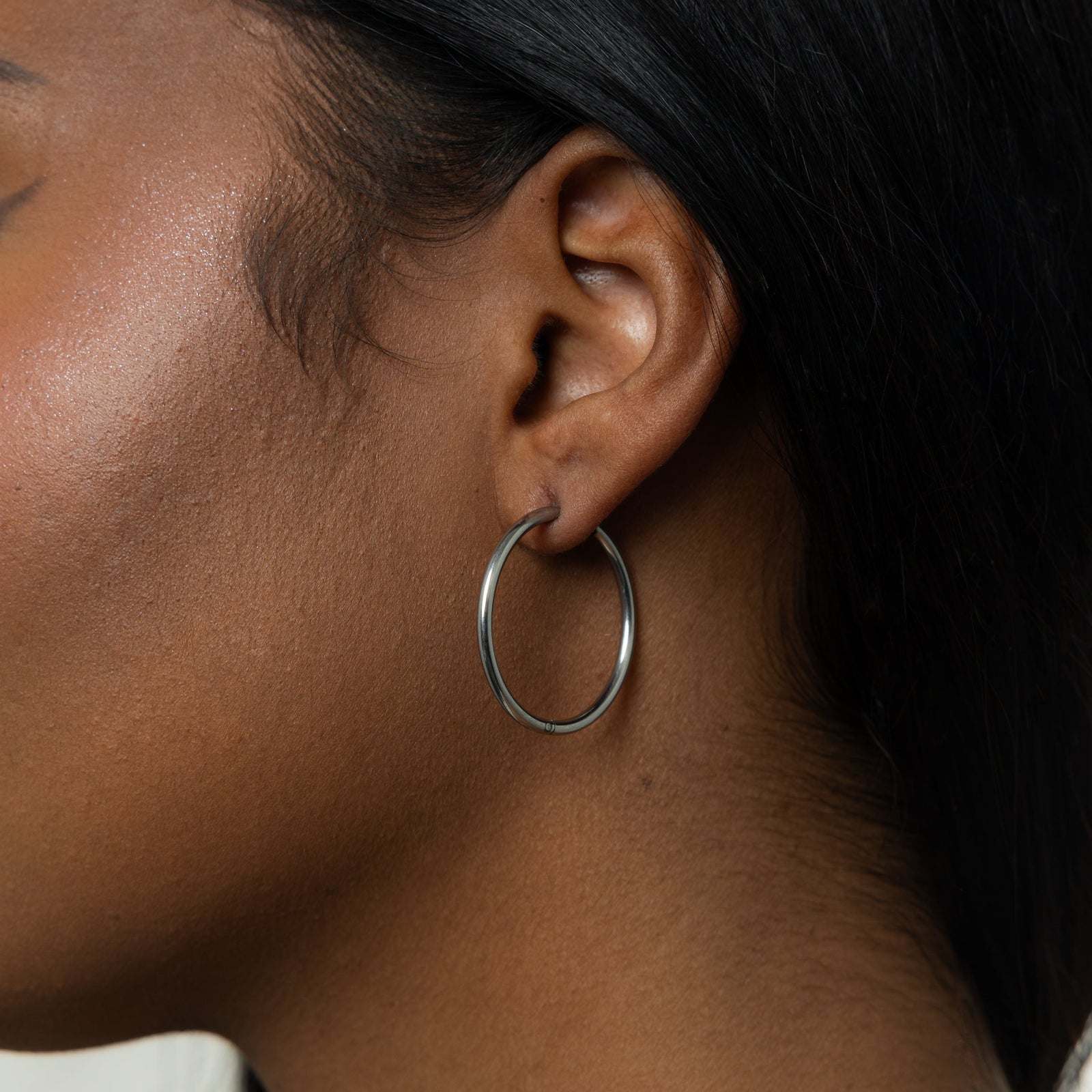 Close up of the silver Large Essential Hoops | 25mm as worn by the model on their left ear.