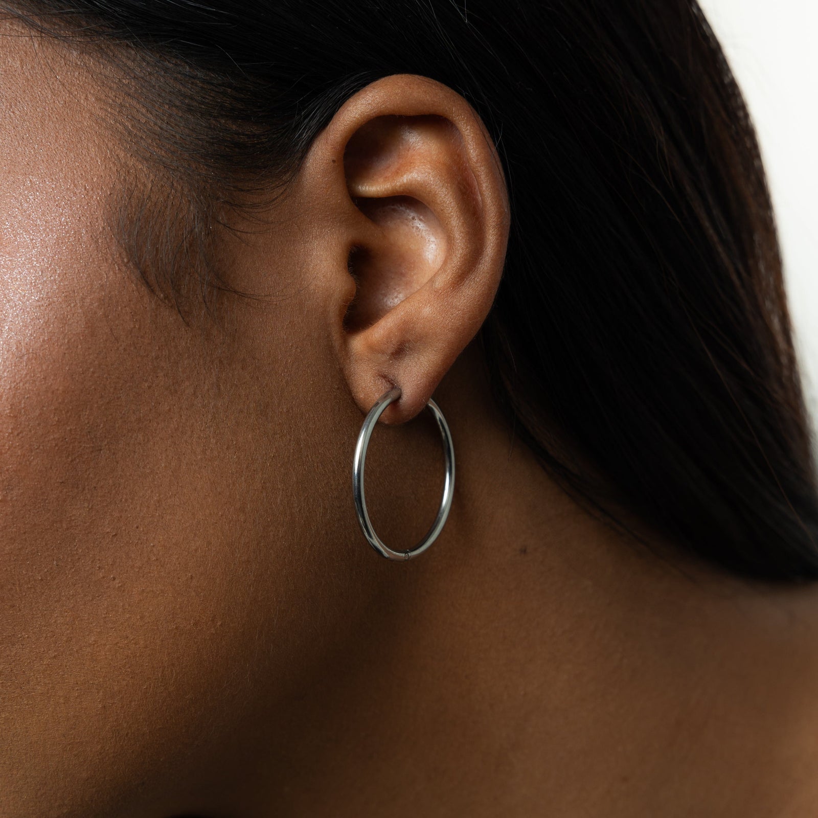 Close up of the silver Large Essential Hoops | 25mm as worn by the model on their left ear.