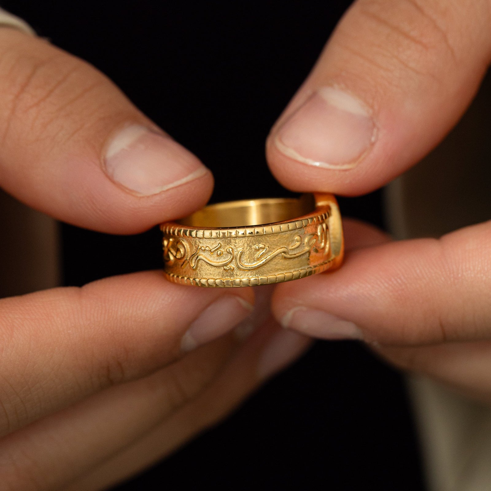 Close up of model holding the ring showing the Arabic calligraphy inscription around the band of the gold ring.