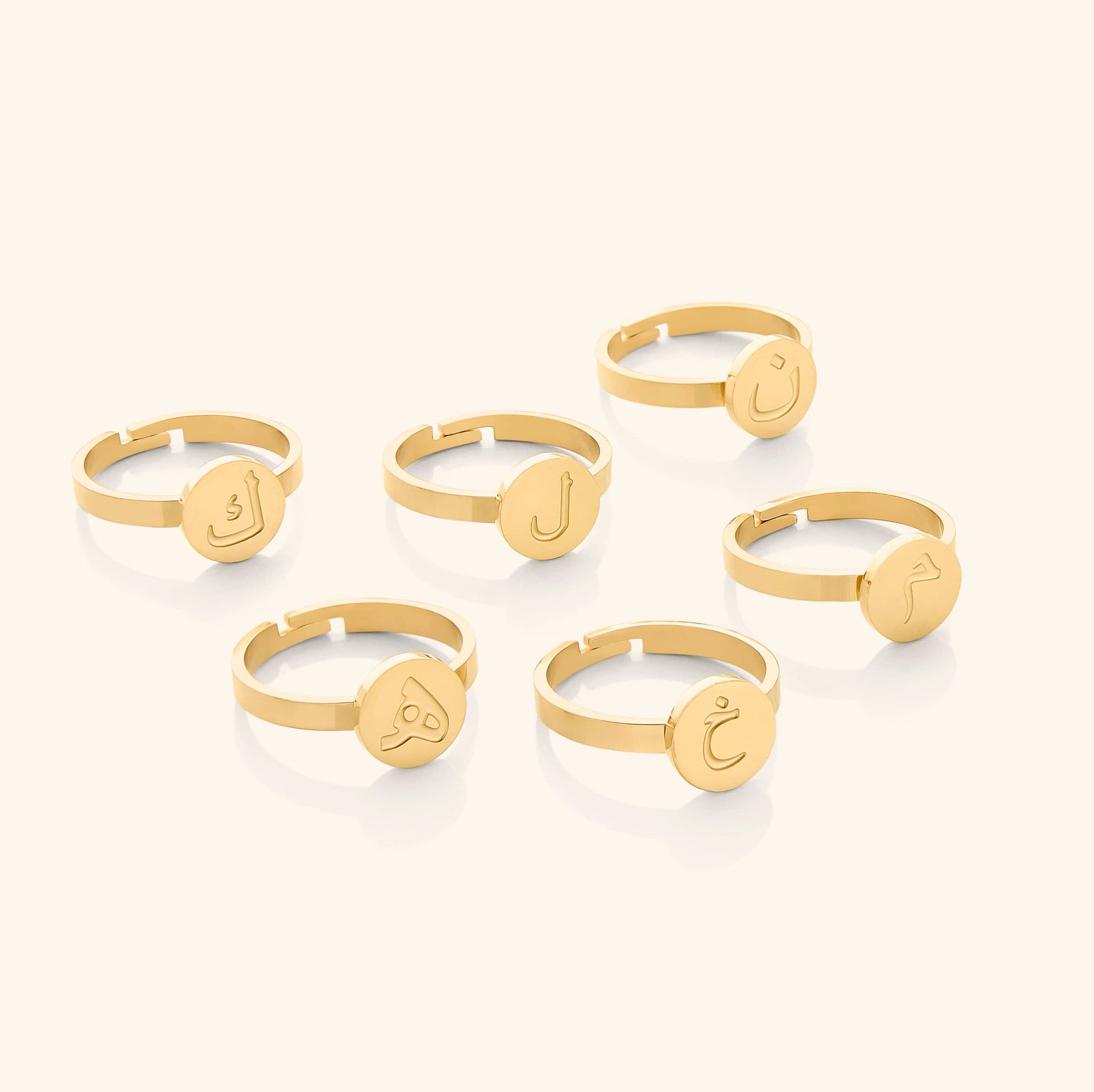 Six gold rings displayed flat lay, each with a round face engraved in Arabic letters