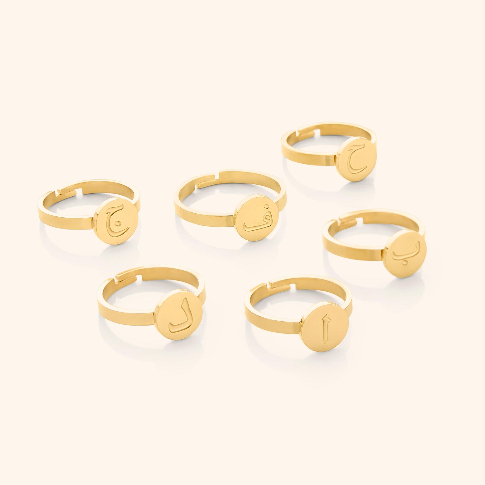Six gold rings displayed flat lay, each with a round face engraved in Arabic letters