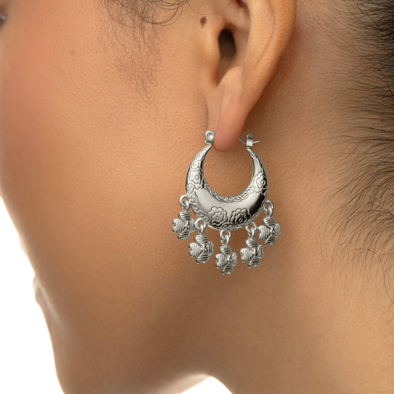 Silver Levantine Garden Hoop Earring with engraved floral details and hanging charms worn on a woman’s ear.
