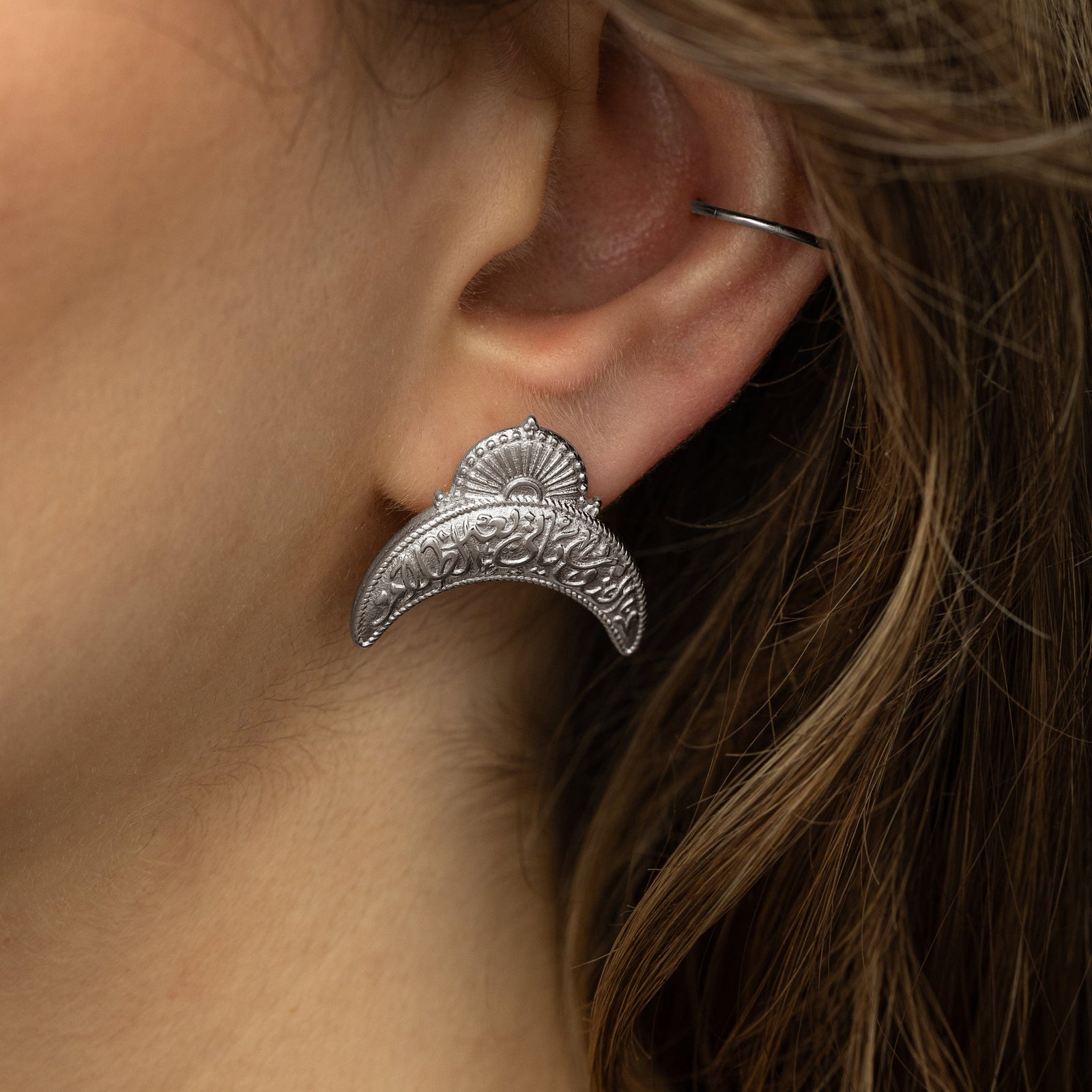Close up of the silver earring as worn by a model.