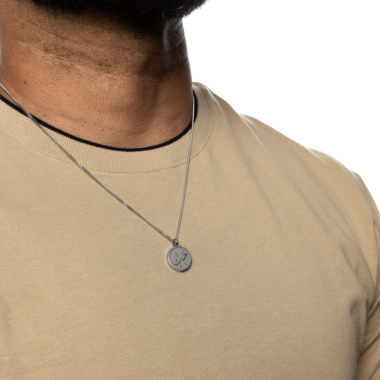 Man wearing a silver love token necklace over a beige shirt.