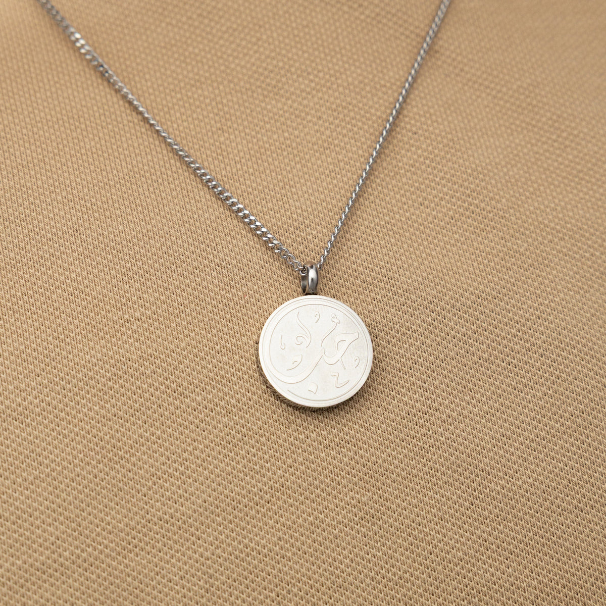 Silver love token necklace worn over a beige textured shirt.