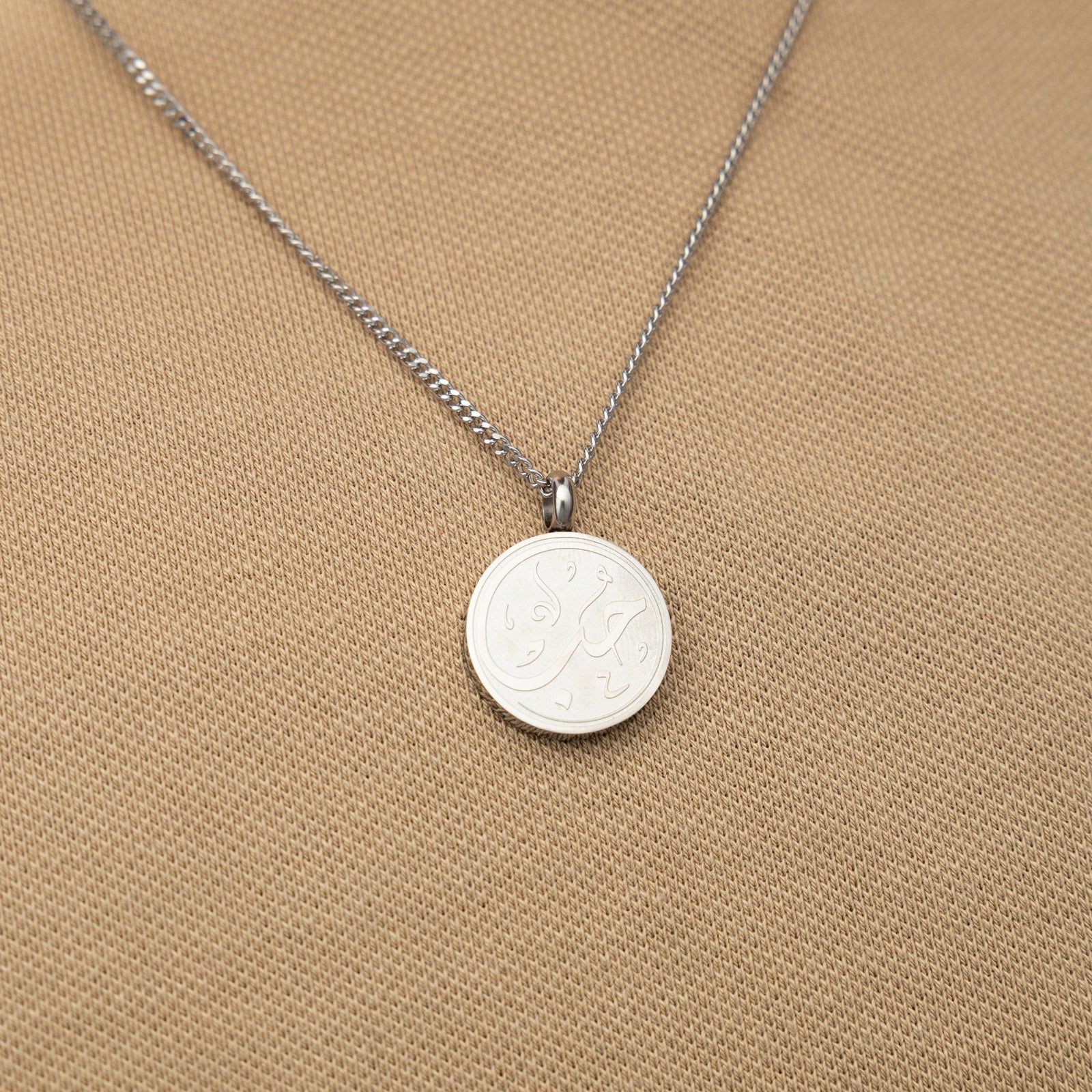 Silver love token necklace worn over a beige textured shirt.
