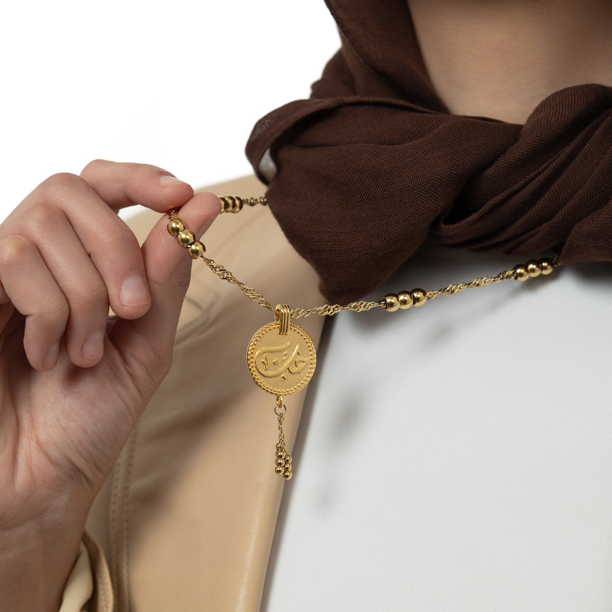 Close up of the gold "Love" Vintage Coin Necklace. The model holding the chain up to show the pendant.