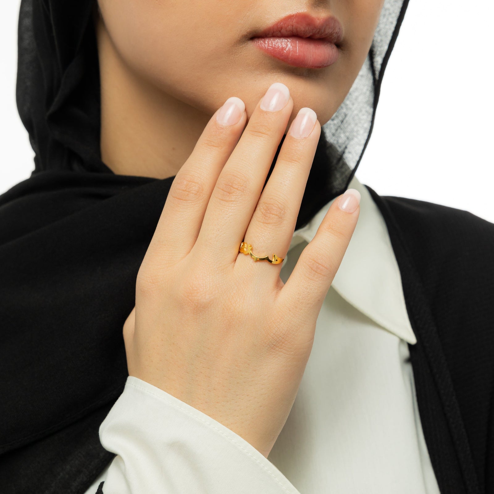 Woman wearing a black hijab with a gold "Love Yourself First" ring, hand lifted near chin.