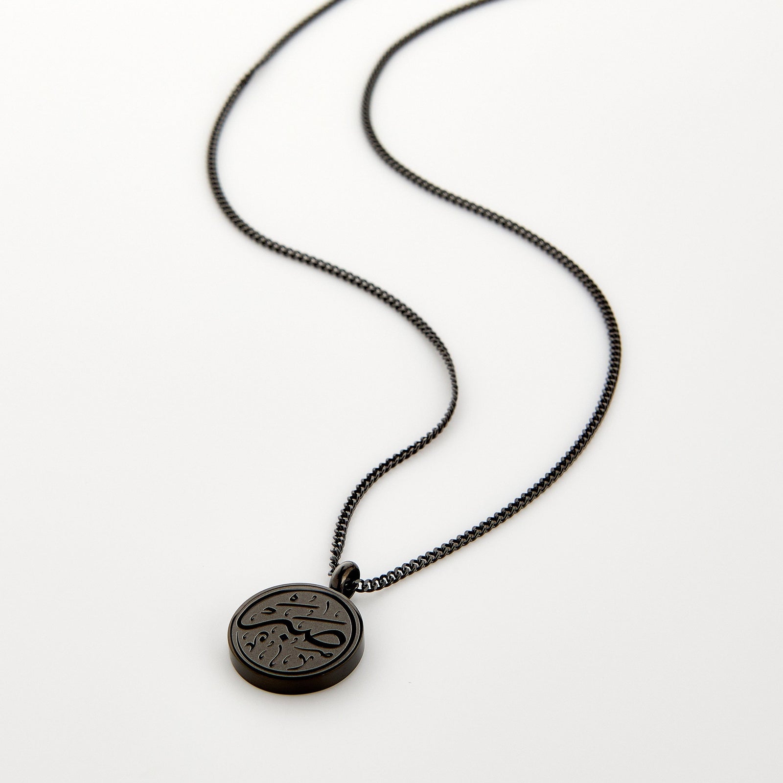 Black necklace with a circular 'Sabr' calligraphy engraved pendant, displayed on a white background.