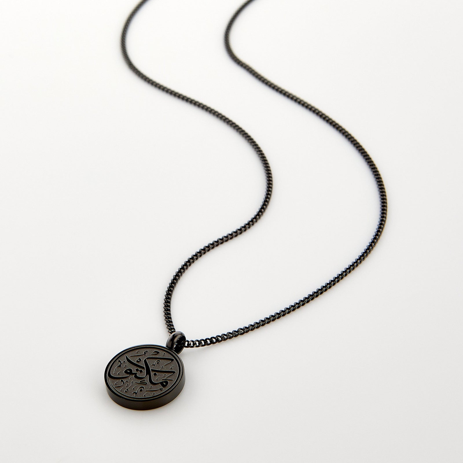 Black necklace with a circular pendant engraved with 'Maktub' calligraphy, displayed on a white background.
