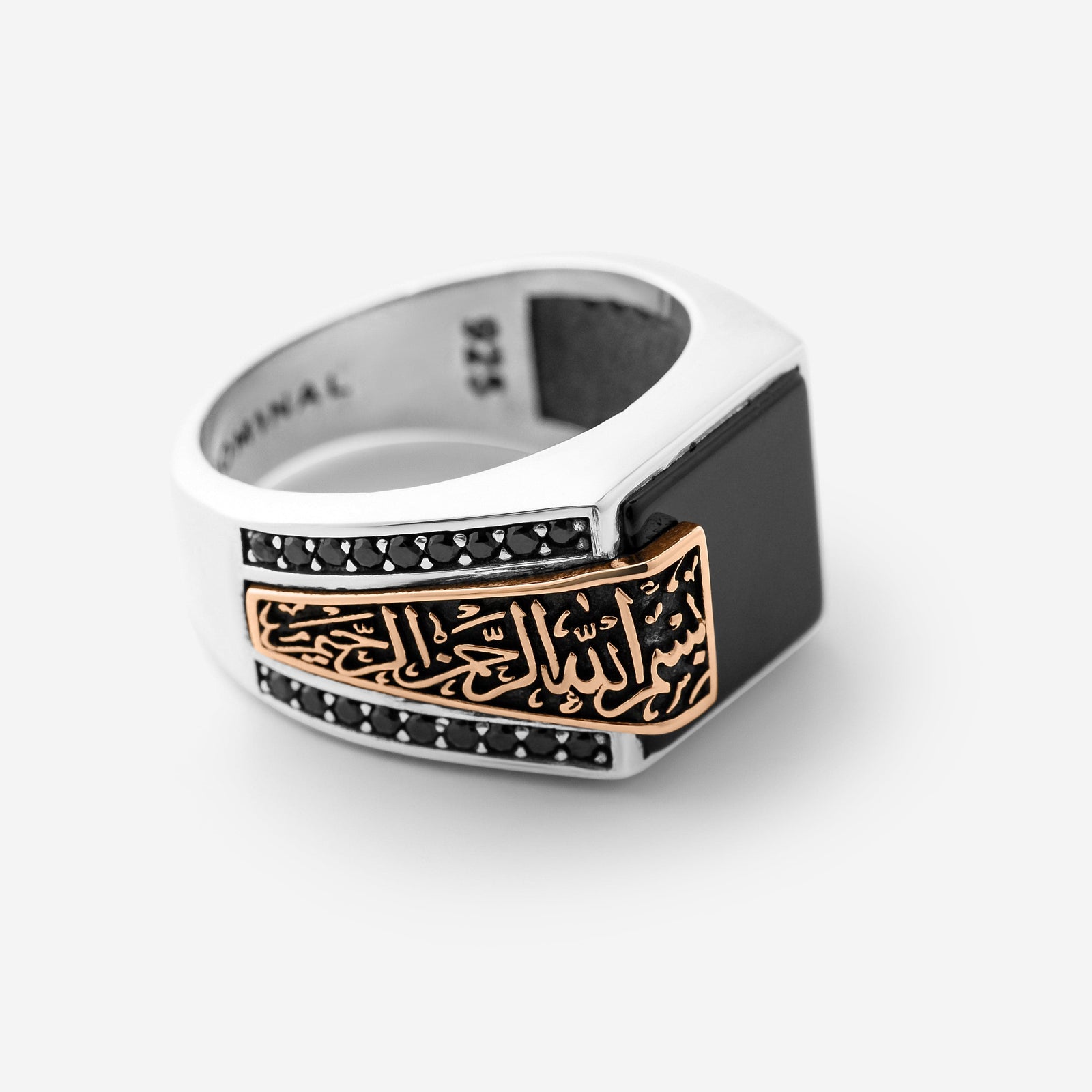 Photo of a ring that features a striking square black Onyx stone anchors this statement piece, with “بِسْمِ اللهِ الرَّحْمٰنِ الرَّحِيْم” (Bismillāhir-Raḥmānir-Raḥīm) engraved in an encased calligraphy that spills from the band onto the stone itself. On the opposite side, “الحمدُ لله” (Al-ḥamdu lillāh) is carved into the band.