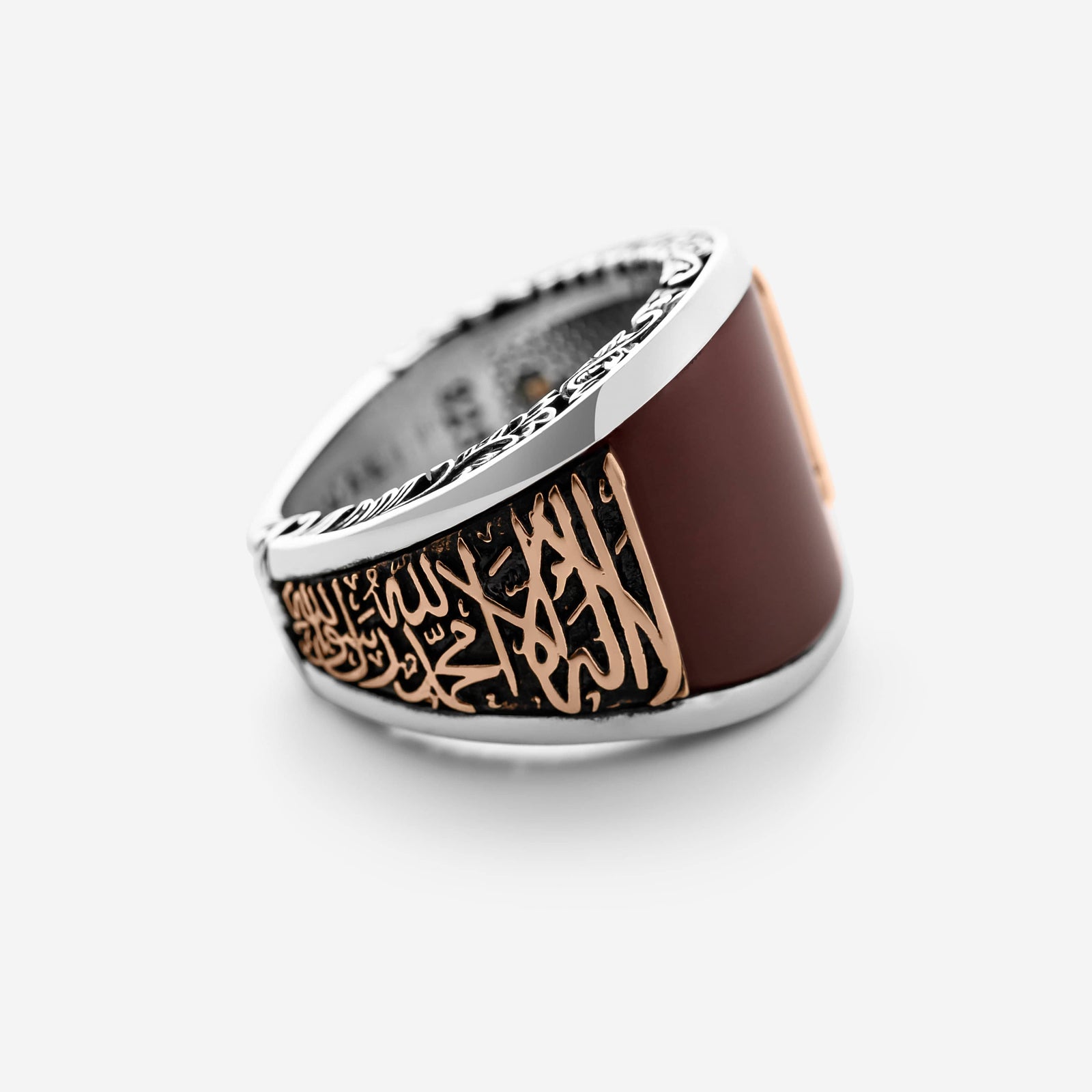 Me's silver ring that features a smooth rounded natural Red Agate stone, surrounded with bronze-toned calligraphy. Along the band, the Shahada, the declaration of faith, is embossed in elongated Arabic script, rising from the ring design.