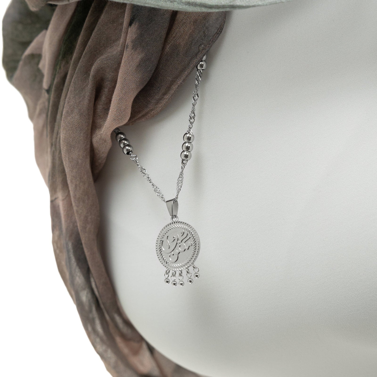 Close up of the Silver "Maktub" Vintage Coin Necklace against the white fabric of the model's clothing. The model is adjusting the the silver necklace and then smiling to the camera.