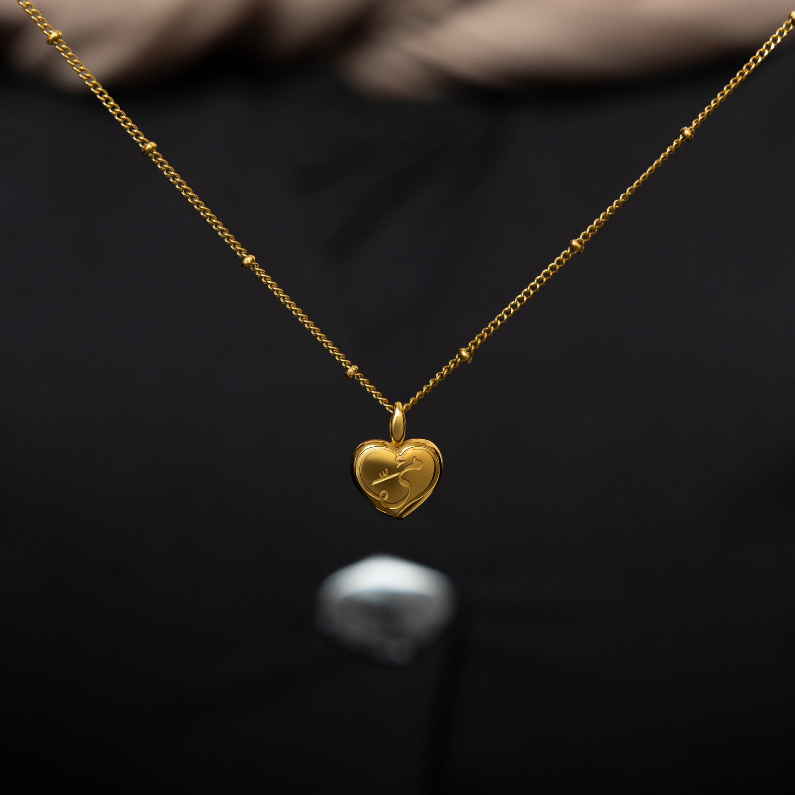 The gold Mama Heart Charm hanging from a thin gold dotted chain.