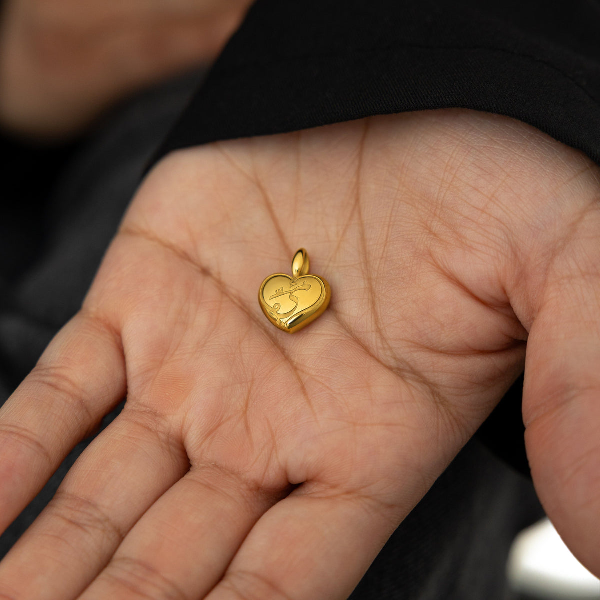close up of the gold Mama Heart Charm on the palm of the model's hand.