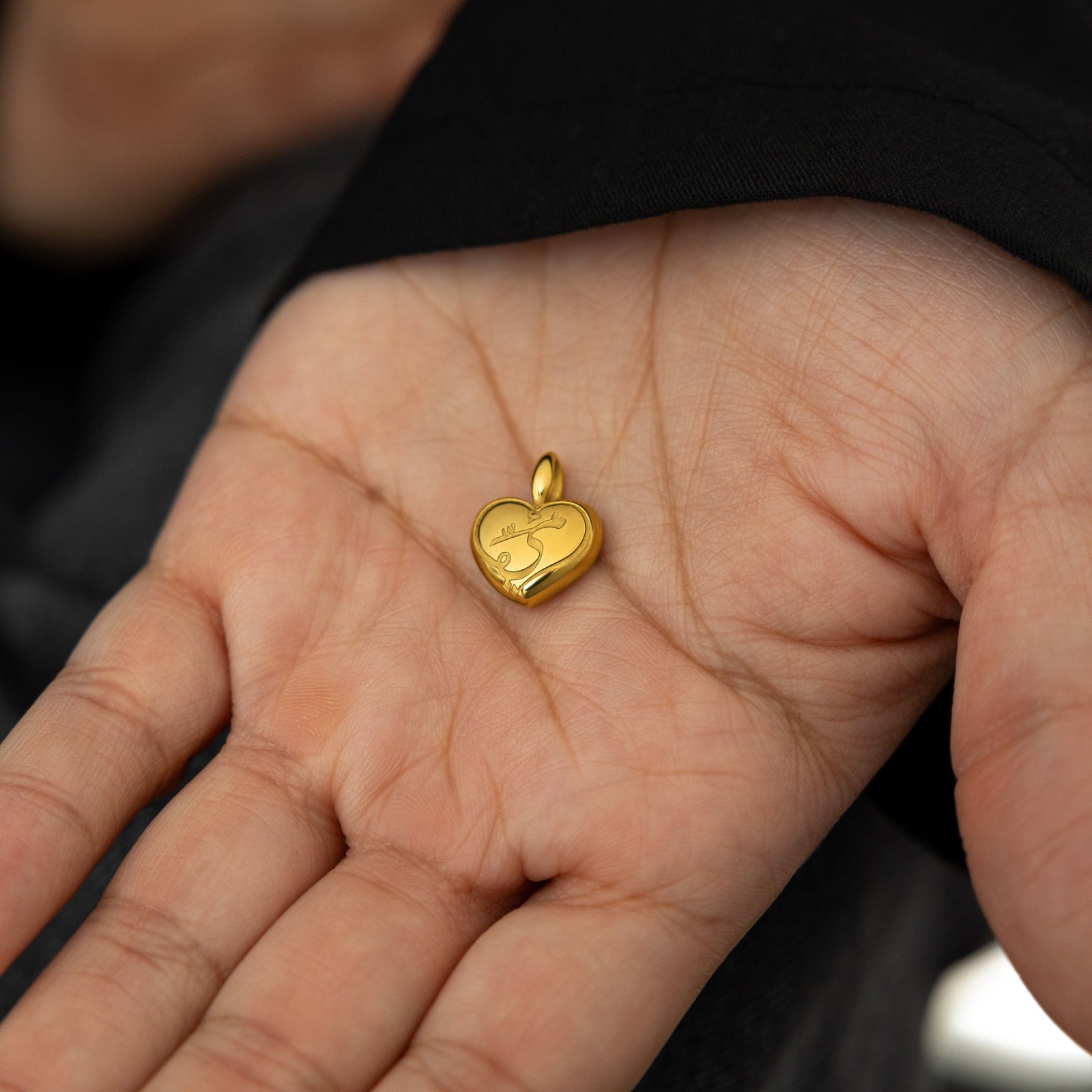 close up of the gold Mama Heart Charm on the palm of the model's hand.